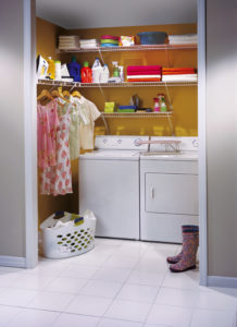 A laundry room with a washer, dryer, shelves stocked with cleaning supplies, and hanging garments.