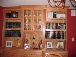 An oak bookcase filled with books, cds, framed photographs, and decorative items in a room with red walls.