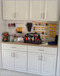 A well-organized workshop area with tools neatly arranged on a pegboard above a white cabinet counter.