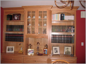 A wooden bookcase filled with books, decorative items, and framed photos against a red wall.