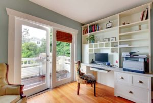 A well-lit home office with built-in shelving, a desk with computer equipment, and a sliding door leading to an outdoor area.