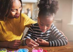 Mother and daughter engaging in a craft activity with beads at home.