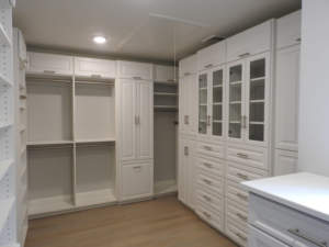 A modern walk-in closet with white cabinetry and shelving units.