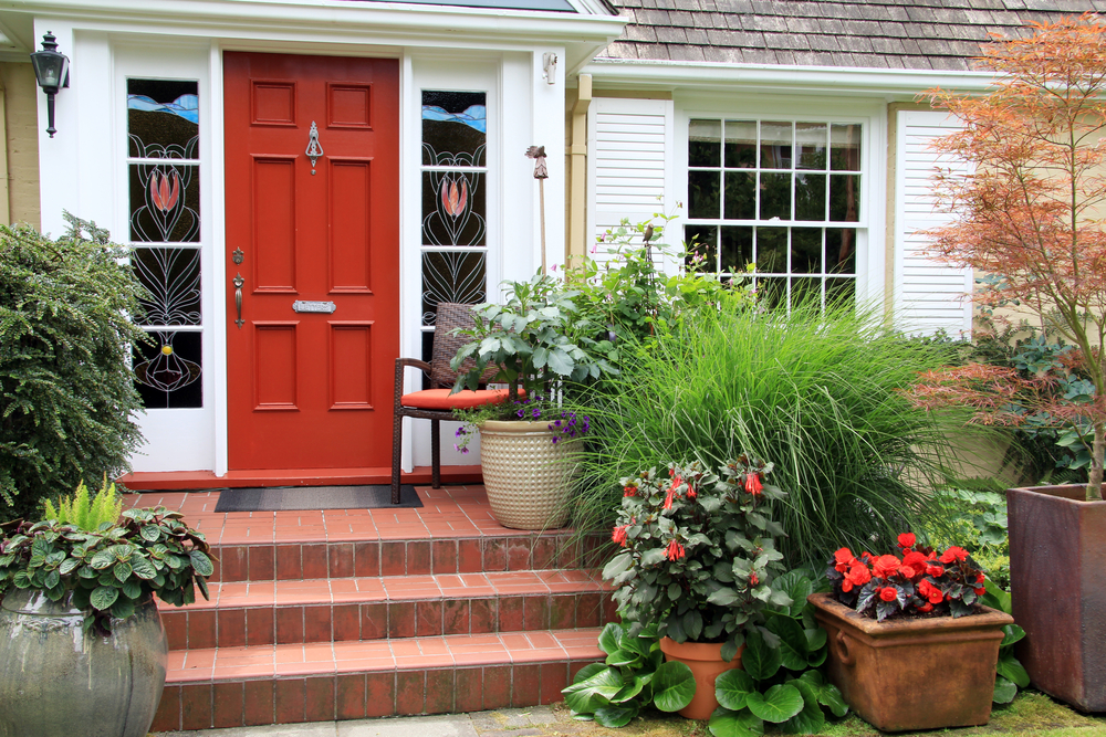 A welcoming house entrance with a red door, white walls, and assorted potted plants on the porch.