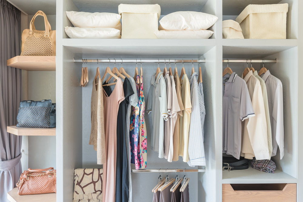 A neatly organized closet with clothing items hung on racks and shelves with bags and pillows.