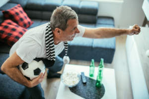 Man gesturing while holding a soccer ball, with snacks and drinks on the table beside him.