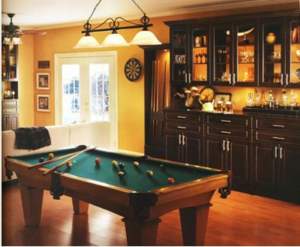 A cozy custom man cave with a pool table, dartboard, and wooden cabinets.