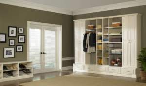 An elegant, well-organized walk-in closet featuring white cabinetry and storage spaces in a room with green walls and framed pictures.