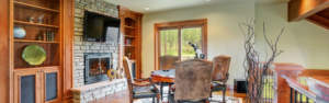 Cozy living room with stone fireplace, mounted television, and a dining area overlooking the outdoors, perfect for custom man caves.