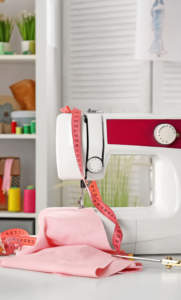 Sewing machine with pink fabric and measuring tape on a craft room table in Boston.