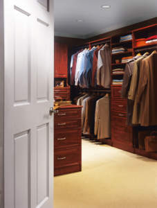 A well-organized walk-in closet featuring Barnstable Closet Design, with wooden cabinetry and a collection of hanging clothes.