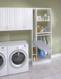A well-organized laundry room with a front-loading washer and dryer, shelving unit containing supplies, and an ironing board.