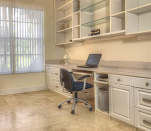 A well-lit home office with a laptop on an office desk, built-in shelving, and a window with blinds.