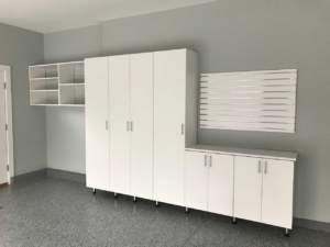 A modern, minimalist office space with white storage cabinets and shelves against a grey wall.
