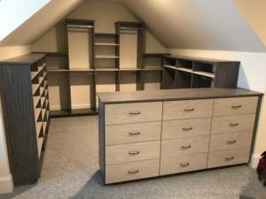 A spacious attic room with built-in shelves and a large wooden chest of drawers.