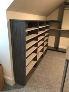 A modern, custom-built shelving unit designed to fit under a sloped ceiling, featuring a combination of open shelves and closed compartments.