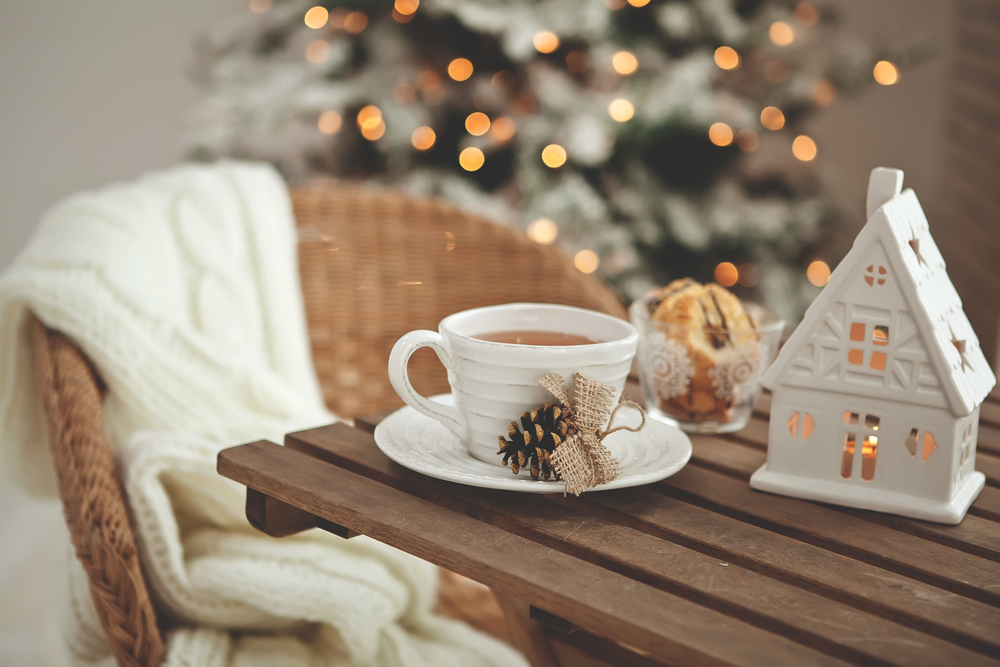 A cozy winter scene with a cup of hot tea, a decorative lantern, and a christmas tree in the background.