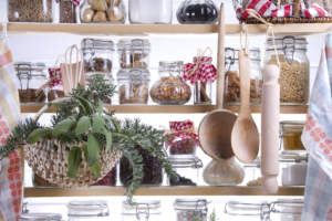 A pantry shelf organized with various labeled jars of spices and dry goods, kitchen utensils, and a potted plant.