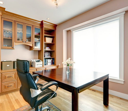 A bright and tidy home office with a large wooden desk, black office chair, and built-in shelving.