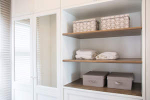 A neatly organized closet with towels and decorative storage boxes on wooden shelves.