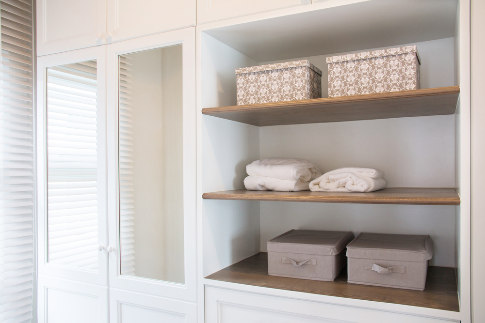 A neatly organized closet with towels and decorative storage boxes on wooden shelves.