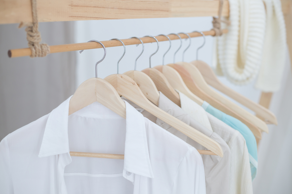 Assorted shirts hanging neatly on wooden hangers in a bright, airy closet space.