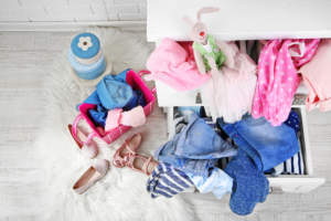 A drawer filled with children's clothing items and a toy rabbit, with additional clothes and shoes scattered on a white fluffy rug.