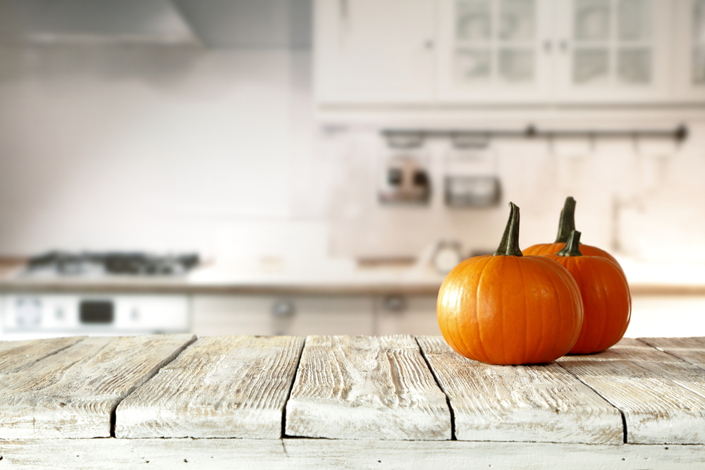 Two pumpkins on a rustic wooden table with a blurred kitchen background.