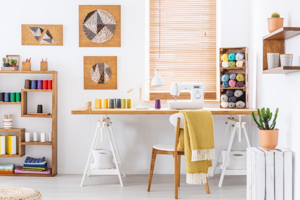 A tidy and well-organized craft room with a sewing machine, fabric, and yarn on shelves.