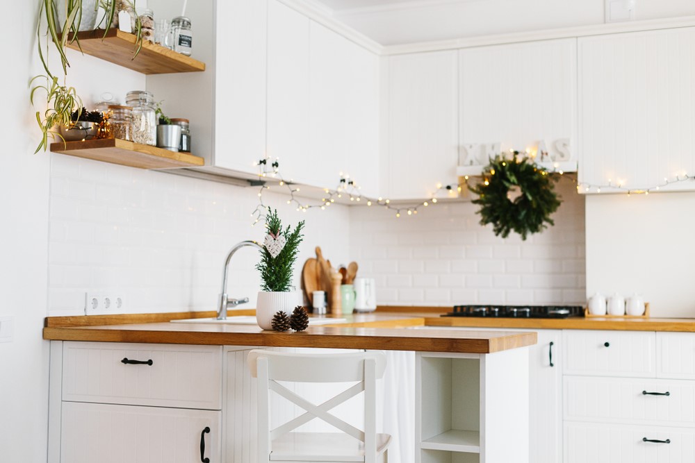 A clean and bright kitchen interior with wooden countertops, white cabinetry, and decorative greenery.