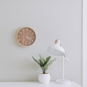 A minimalist workspace with a wooden wall clock, a custom closet, and a potted plant.