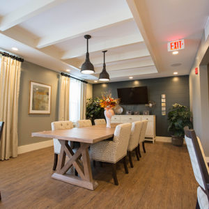 A modern dining area with a wooden table, wicker chairs, pendant lights, and a custom closet next to the door with an exit sign above.