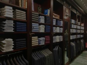 Elegant men's clothing store interior with neatly arranged shirts and suits on wooden shelves.