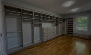 Empty walk-in closet with built-in shelves and drawers, parquet flooring, and natural light from a window.