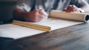 A person drafting custom closet plans on paper with a ruler and pen on a wooden desk.