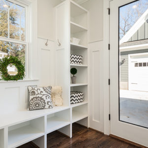 A bright entryway featuring custom closet white built-in storage units with hooks, shelves, and a bench with decorative cushions.