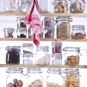 Assorted dry goods organized in glass jars on white shelves in a custom closet.