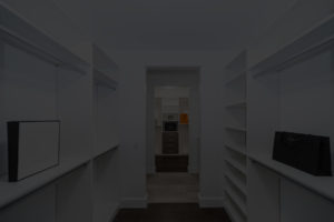 A dimly lit, custom closet with white shelves and two designer shopping bags.