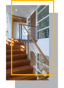 Modern wooden staircase with glass and metal railing in a bright interior featuring a custom closet.