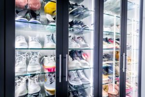 A variety of sneakers neatly displayed in a lit glass cabinet for shoe storage.