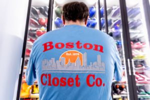 Man in a "boston closet co." shirt facing a well-organized display of colorful helmets.
