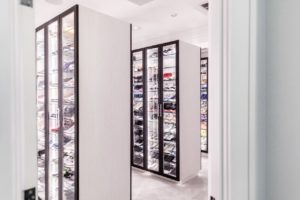 A well-organized walk-in closet with a collection of shoes displayed on shelves behind glass doors.