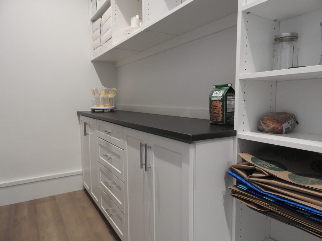 A modern pantry with white shelving, a black countertop, and various pantry items.