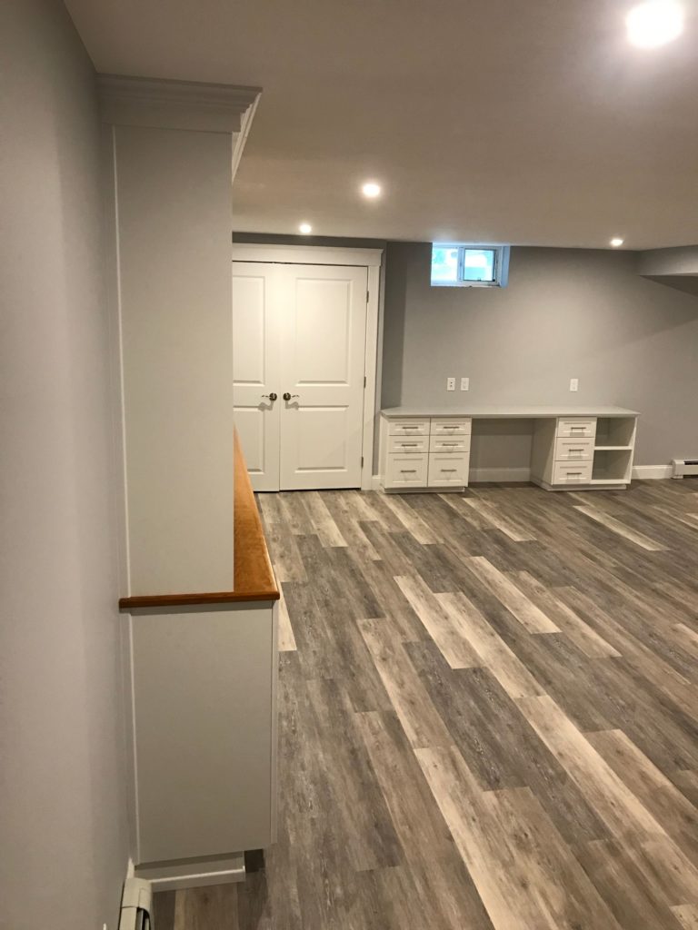 An empty, well-lit basement office with gray flooring and white built-in storage units.