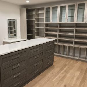 A modern, empty walk-in closet featuring a central island with drawers and surrounding shelves and cabinets.