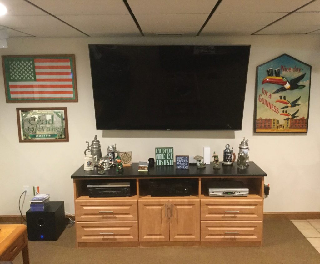 Home entertainment area with a large TV, wooden cabinet, and decorative signs and items on the walls, designed as custom man caves.