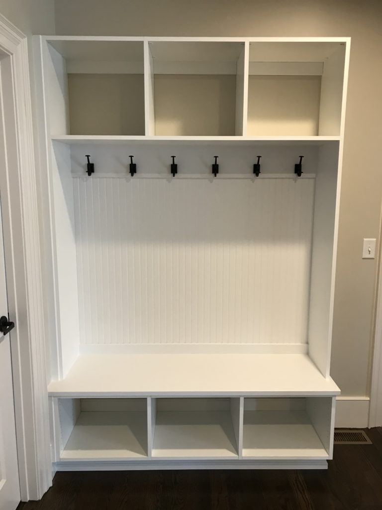 White mudroom organizers with bench, cubbies, and coat hooks.