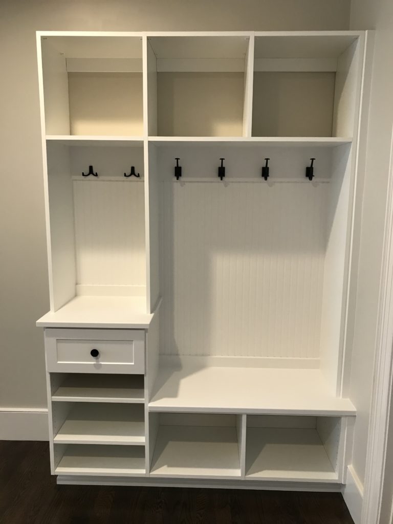 White built-in mudroom organizers with bench, hooks, and shelves.