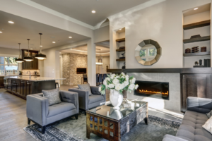 Modern open-concept living room with kitchen view, featuring a fireplace, elegant furnishings, and pendant lighting.