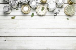 Canned food and a can opener arranged on a wooden surface.